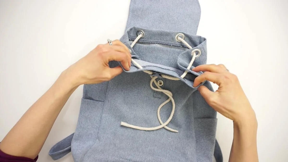 To finish the DIY backpack, insert the cord through the eyelet hole and the drawstring tunnel to adjust the opening of the bag.