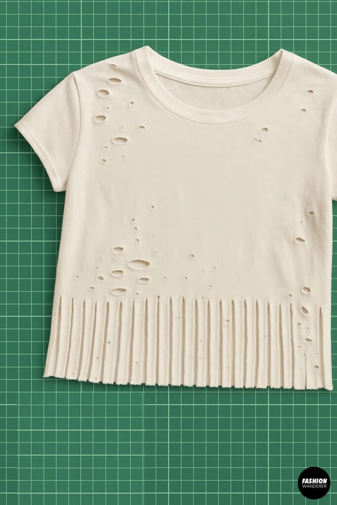 Finished DIY distressed crop top featuring fringe hem and scattered holes across the top — laid flat on a green cutting mat for a clean reveal.