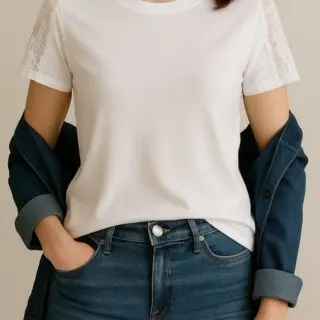 Woman wearing a fitted white T-shirt with lace inserts on the sleeves, styled casually with dark blue jeans and a denim jacket draped off the shoulders.