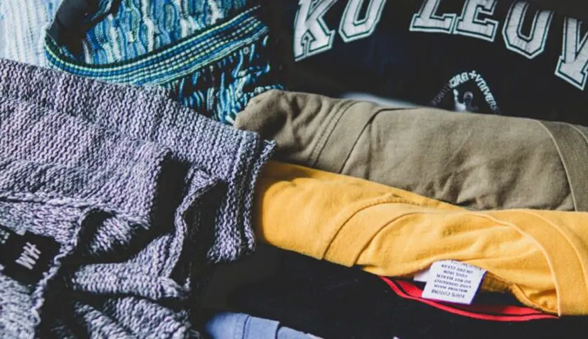 Stack of folded clothes including cotton, knitwear, and graphic T-shirts in various textures and colors like olive, yellow, and blue