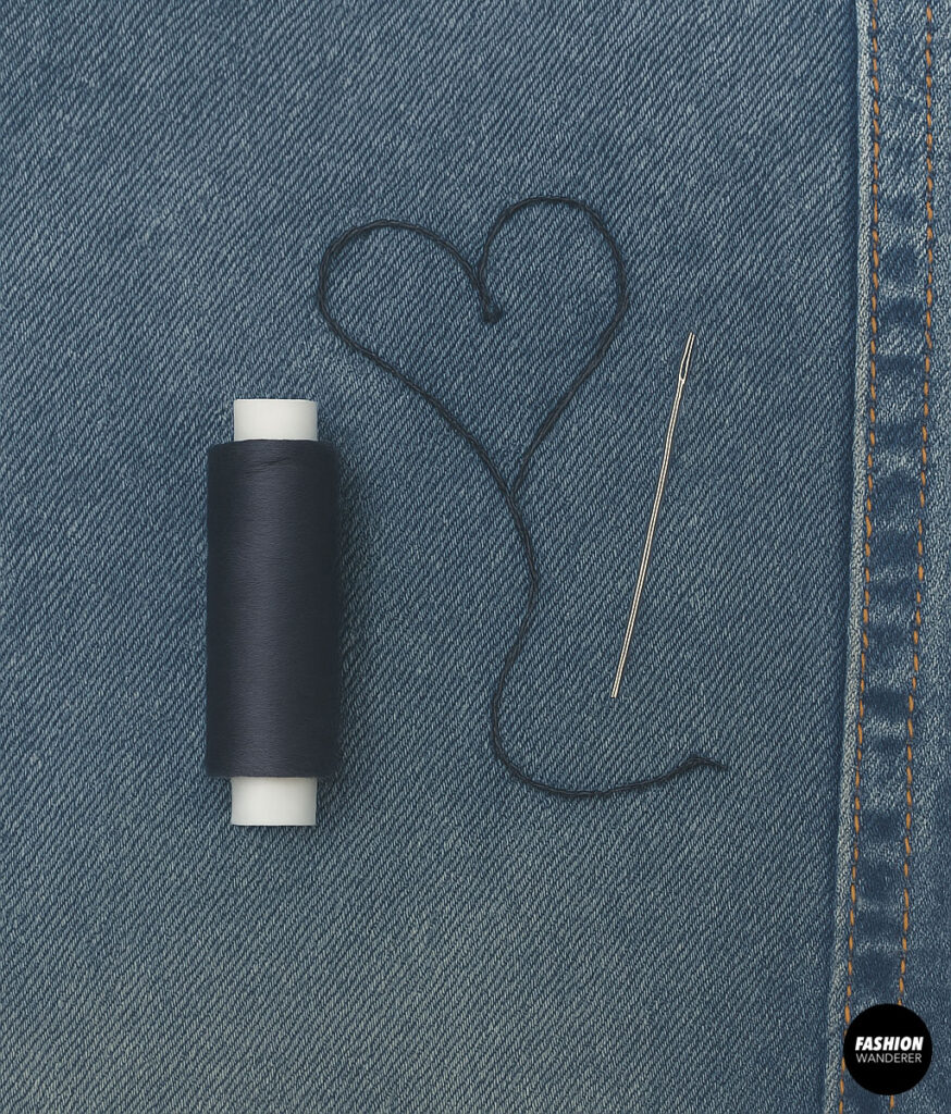Aesthetic flat lay of black thread, needle, and stitched heart shape on denim background, representing love for hand sewing and embroidery.
