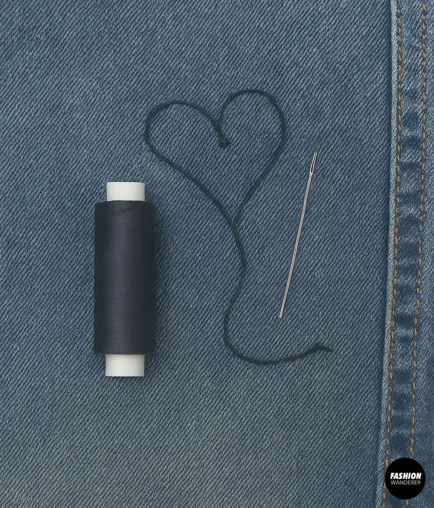 Aesthetic flat lay of black thread, needle, and stitched heart shape on denim background, representing love for hand sewing and embroidery.