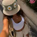 Top view of woman wearing a crochet daisy bucket hat with white tank top and beige summer shorts.