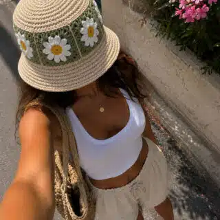 Top view of woman wearing a crochet daisy bucket hat with white tank top and beige summer shorts.
