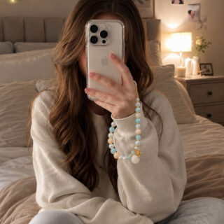 Woman wearing a sweatshirt and sweatpants taking a selfie in a bedroom with a coastal charm beaded wristlet attached to the smartphone.