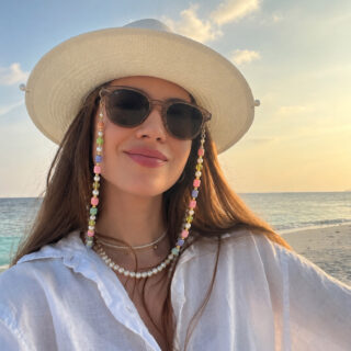 Woman at the beach wearing a sunhat with sunglasses and a chunky beaded sunglass chain.
