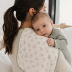 Baby boy in a sage green onesie resting on a handmade floral burp cloth draped over his mother’s shoulder.