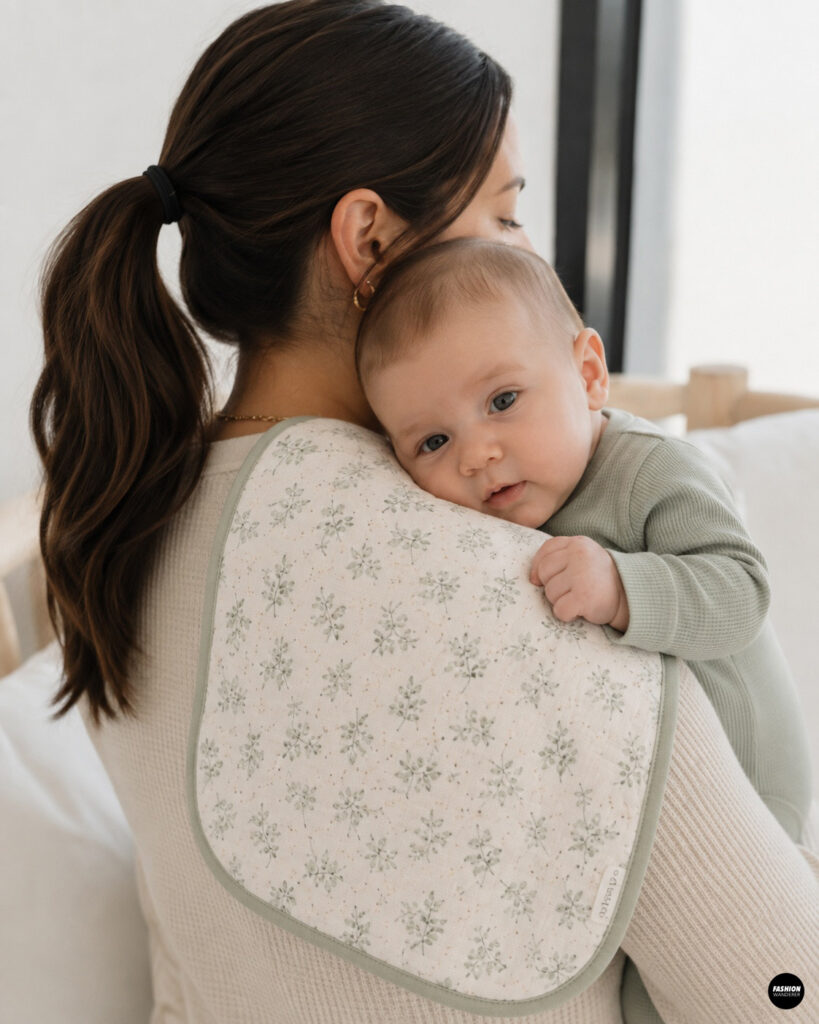 Baby boy in a sage green onesie resting on a handmade floral burp cloth draped over his mother&rsquo;s shoulder.