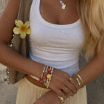 Woman wear a white tank top and beige ribbed bottom with a shoulder purse and summer fruit beaded charm bracelets.