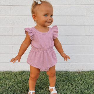 Toddler girl wearing a soft pink ruffle-sleeve romper made from an upcycled T-shirt. The knit romper features flutter sleeves, an elastic waist, snap crotch closure, and white sandals, making it a comfortable outfit for everyday play.