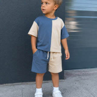 Toddler boy modeling a two-tone blue and cream color-block T-shirt and matching shorts set sewn from recycled T-shirts. The casual outfit features a relaxed fit, elastic drawstring shorts, and white sneakers for a modern everyday look.