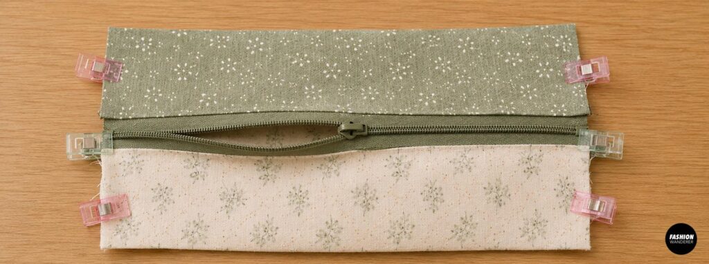 DIY pencil pouch sewing step showing the sage green zipper opened halfway before joining the exterior and lining fabric pieces.