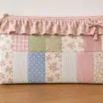 DIY patchwork ruffle zipper pouch made with pastel floral, gingham, striped, and polka dot fabric scraps, finished with a floral ruffle, bow charm, and pink zipper.
