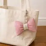 DIY puffy fabric bow bag charm made from pink bow-print cotton with a floral center and swivel clasp, attached to a cream canvas tote bag.