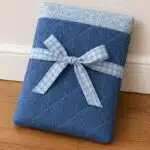 DIY quilted book and Kindle sleeve in blue fabric with floral lining and a gingham bow closure, a beginner-friendly handmade gift and sewing project to sell.