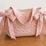 DIY quilted slouchy bow tote bag made with pink floral fabric, diamond quilting, long shoulder straps, and oversized side bows, an easy sewing project to make and sell.
