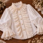 Finished white Victorian ghost blouse with puff sleeves, layered eyelet lace ruffles, pearl buttons, and vintage details arranged on a wooden table with sewing supplies.